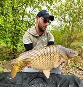 Angler in sunglasses holding a common carp at Alderwood Fishery
