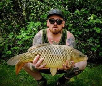 Angler in a cap holding a large common carp at Alderwood Fishery