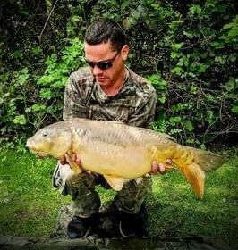 Angler holding a golden mirror carp among the trees at Alderwood Fishery