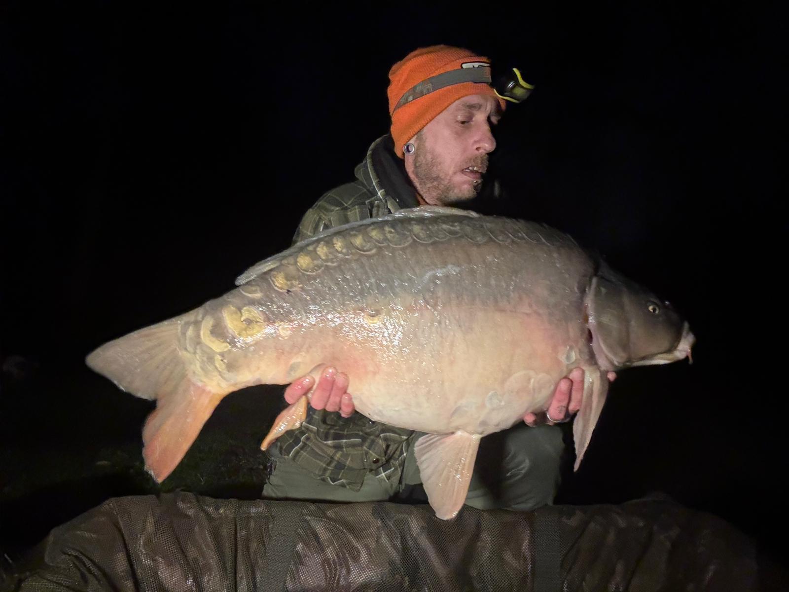 Angler holding a large mirror carp caught at night at Alderwood Fishery
